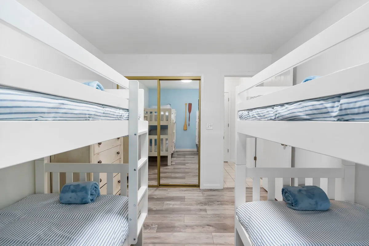 The room contains two twin-over-twin bunk beds with blue towels and a decorative paddle on the wall. The setup is playful and cozy, evoking the excitement of sleepovers and shared adventures for kids.