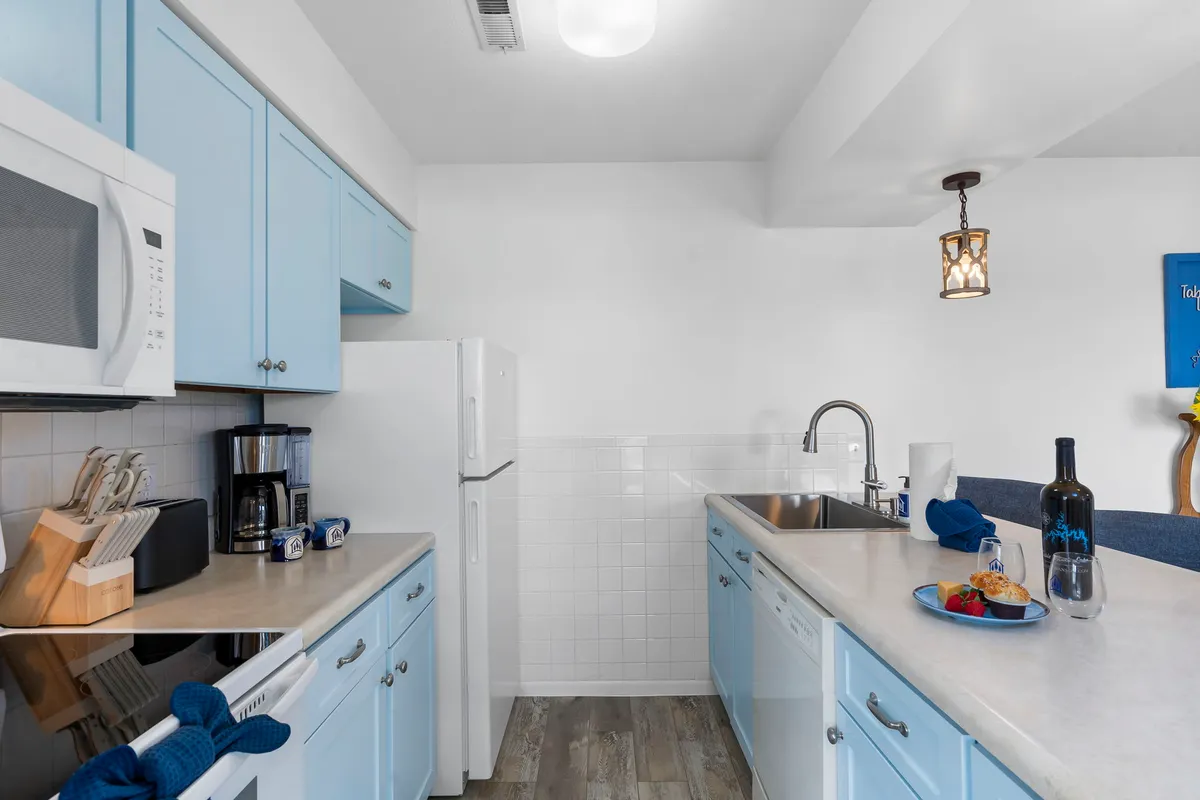 This image showcases a bright, cheerful kitchen with light blue cabinetry, stainless steel appliances, and a kitchen island with bar seating. The countertop is decorated with stylish items, emphasizing a space designed for both cooking and casual gatherings.