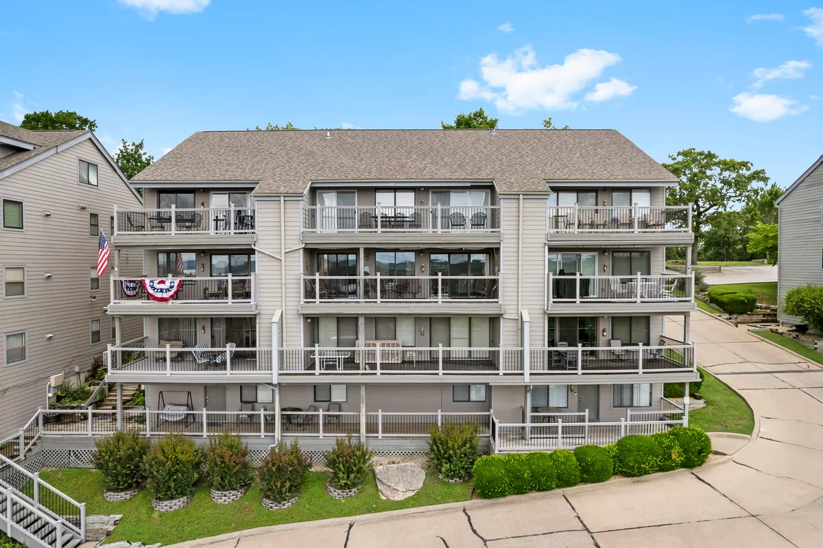 An exterior image featuring balconies with chairs, lush greenery in the foreground, and the building adorned with an American flag. The scene exudes a welcoming, community-oriented feel, ideal for multi-generational groups enjoying the outdoors from accessible balconies.
