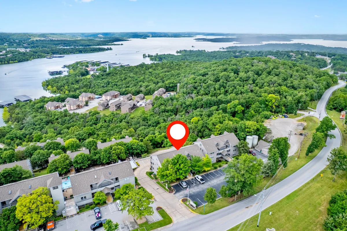 This image showcases lush greenery leading down to a peaceful waterfront, with residential buildings nestled along the shoreline. The scene invites viewers to imagine boating, hiking, or enjoying a picnic while taking in the tranquil lakeside atmosphere.