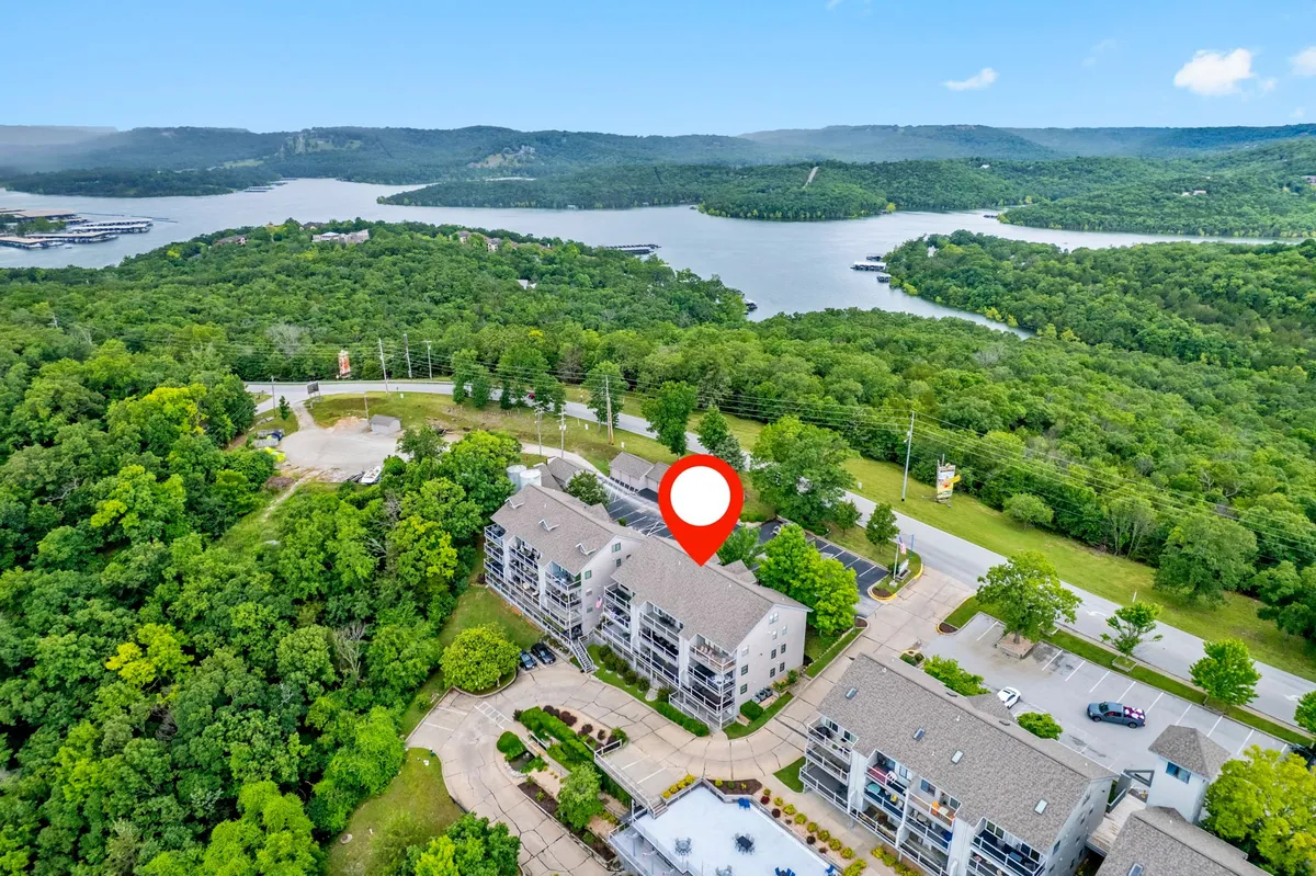 A sweeping view of Table Rock Lake surrounded by lush green landscape and residential buildings, with a roadway leading toward the water. The scene captures tranquil lakefront scenery with hints of recreational activity options like boating, hiking, and relaxing by the shore.