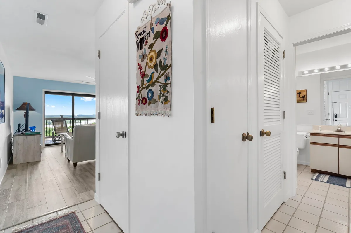 The entryway featuring a colorful wall hanging and a direct view into the living area, revealing light-colored cabinetry and the seamless flow of the space. The layout is open and inviting, with a glimpse of the balcony and outside scenery.