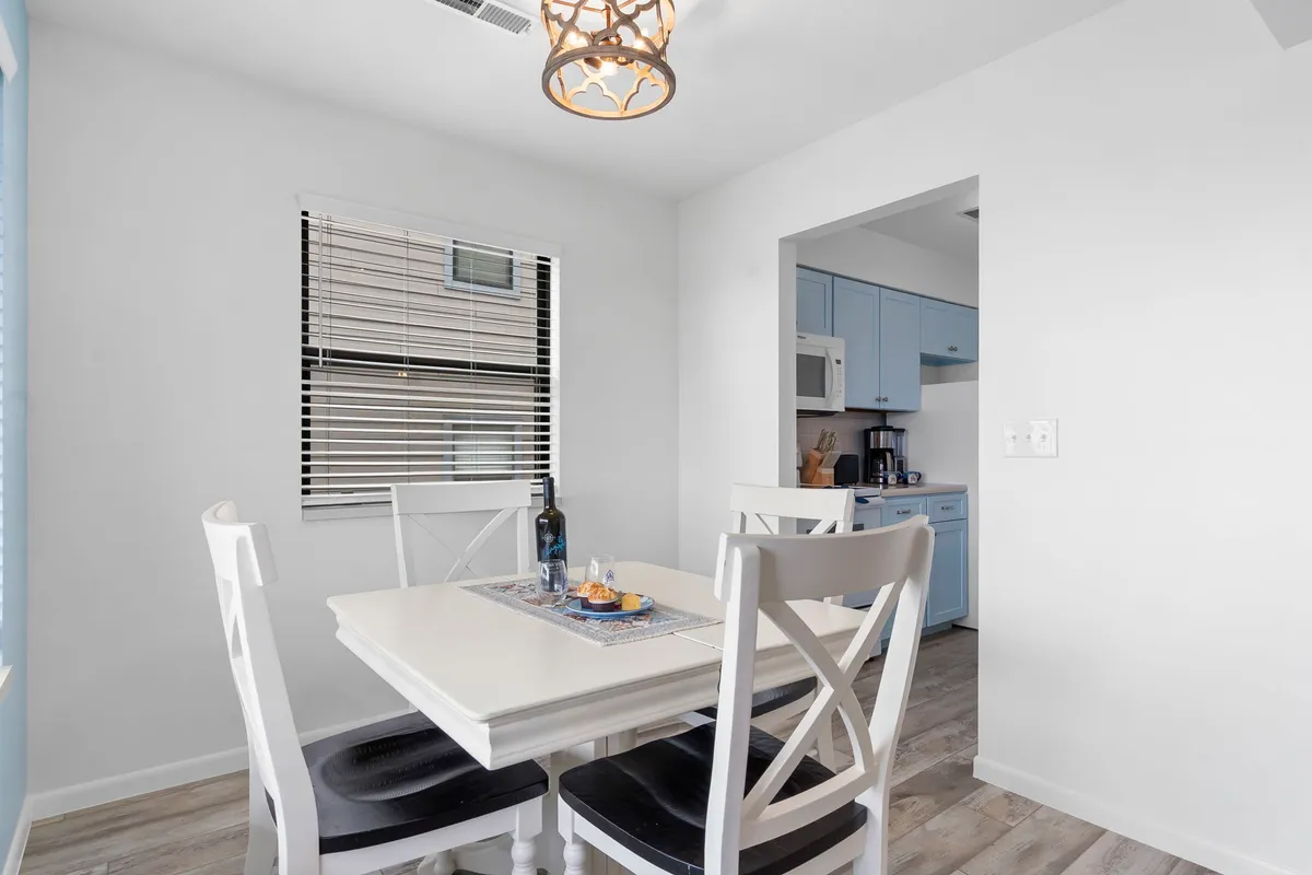 An inviting dining area features a dining table under a chandelier with blue kitchen cabinets in the background. The setup is ideal for family meals, celebrations, and creating shared memories.