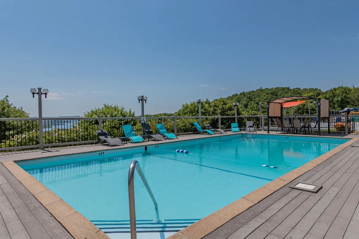 An outdoor swimming pool surrounded by lounge chairs and a cabana, with a landscape view extending beyond. The setting is tranquil, inviting guests to swim, sunbathe, or relax by the pool under open skies.