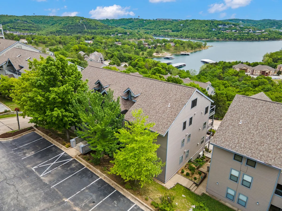 A serene waterfront view framed by lush green trees and modern architectural details in the foreground. The scene suggests access to lakeside strolls, boating, or picnics, with the water gently reflecting the sky and trees. The overall atmosphere is calm and inviting, perfect for connecting with nature or unwinding after exploring Branson.
