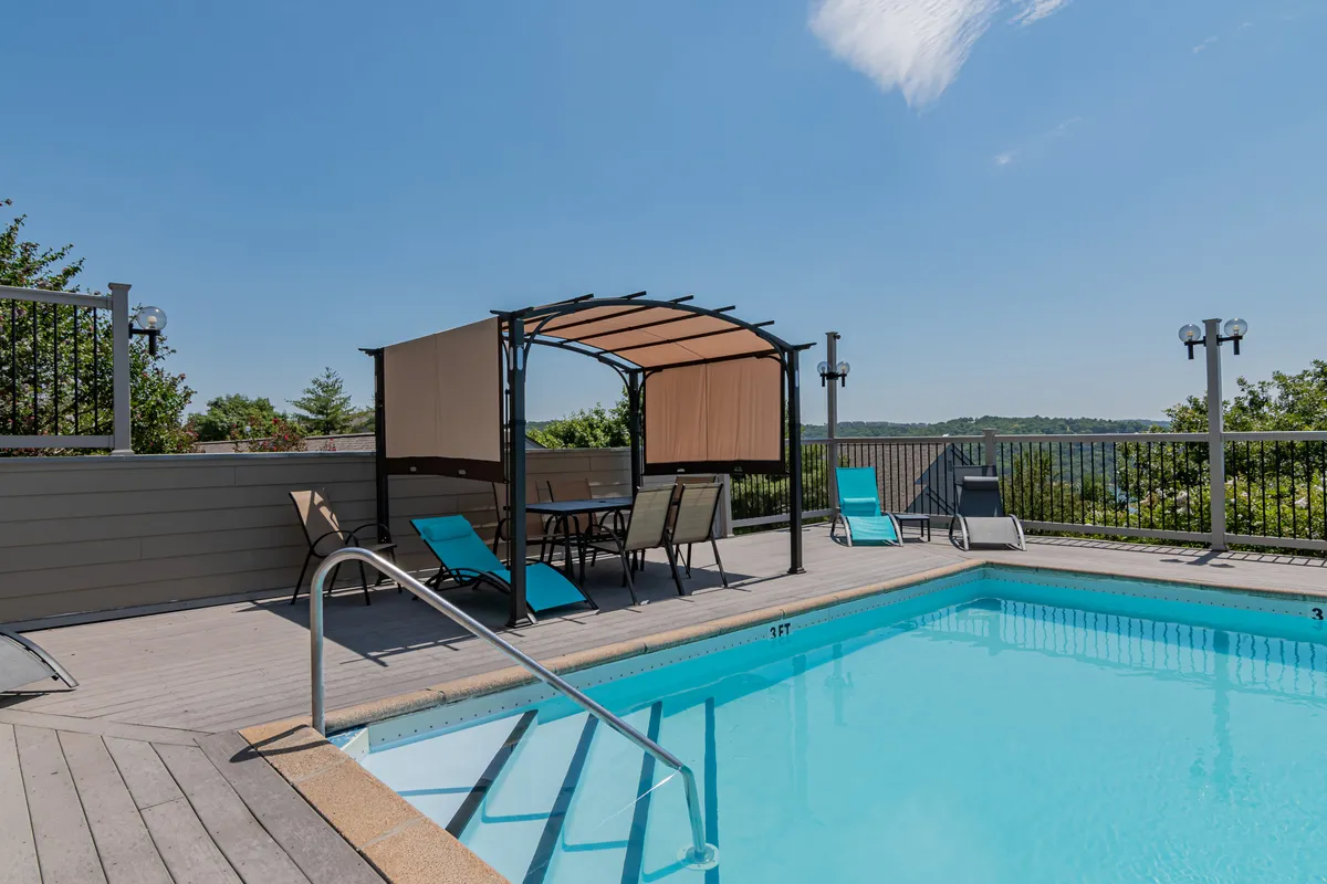 An inviting outdoor swimming pool bordered by a canopy area and lounge chairs, with views extending toward the water. The scene suggests leisurely afternoons, poolside barbecues, and socializing after a day exploring local attractions.