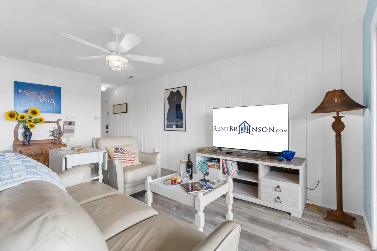 The image showcases a cozy, stylish living room with a plush sofa, a large television, a modern coffee table, warm lighting from a lamp, and tasteful wall art. This inviting space is perfect for relaxing after a day at the lake or nearby attractions, and sets the tone for a comfortable, home-like experience.