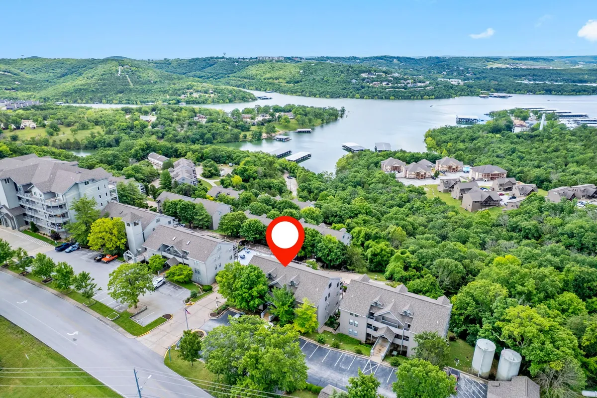A serene lakeside vista framed by lush green trees and modern buildings, suggesting immediate access to the water for boating or lakeside strolls. The light hints at sunset, aligning with the idea of evenings spent enjoying the natural setting.