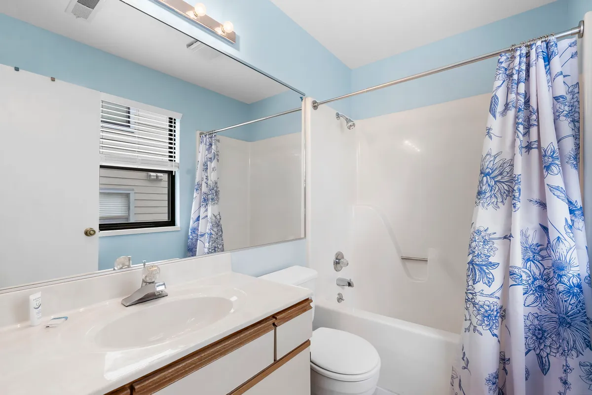 This bathroom features a vanity with sink, a mirror, and a shower area with a floral curtain. The clean and calming design is suited for both refreshing morning starts and relaxing evening routines.